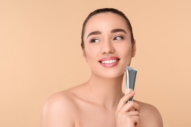 Photo of Woman holding tube of foundation on beige background