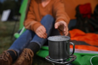 Woman taking cup off stove while sitting in camping tent outdoors, closeup