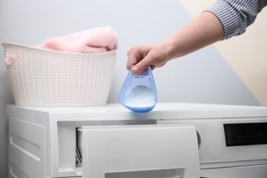 Photo of Woman pouring powder into drawer of washing machine indoors, closeup. Laundry day