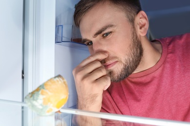 Man smelling stinky stale cheese in refrigerator