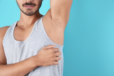 Photo of Young man showing armpit on color background, space for text. Using deodorant