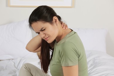 Photo of Young woman suffering from neck pain on bed in bedroom