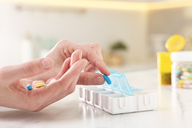 Photo of Woman with pills and organizer at white marble table, closeup