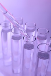 Dripping liquid from pipette into test tube on violet background, closeup