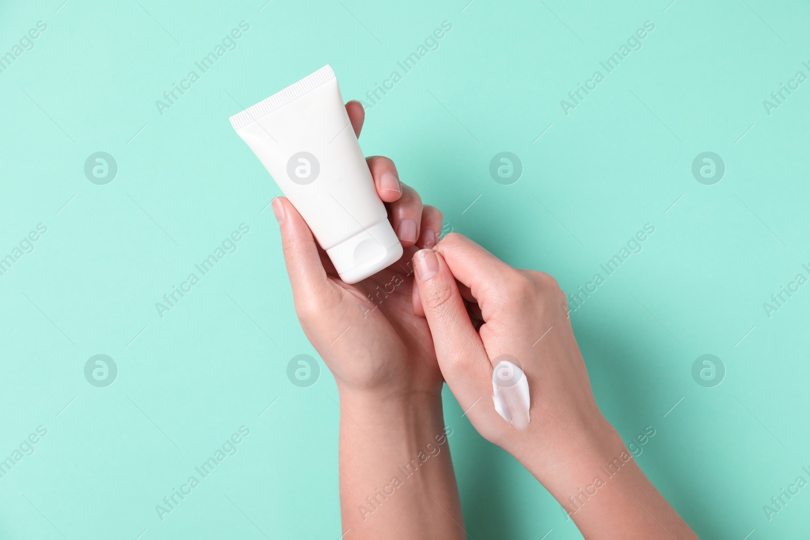 Photo of Woman with tube of hand cream on turquoise background, top view