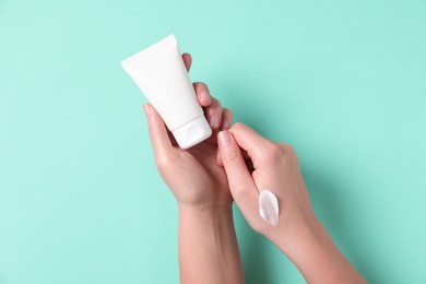 Photo of Woman with tube of hand cream on turquoise background, top view