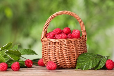 Photo of Wicker basket with tasty ripe raspberries and leaves on wooden table against blurred green background
