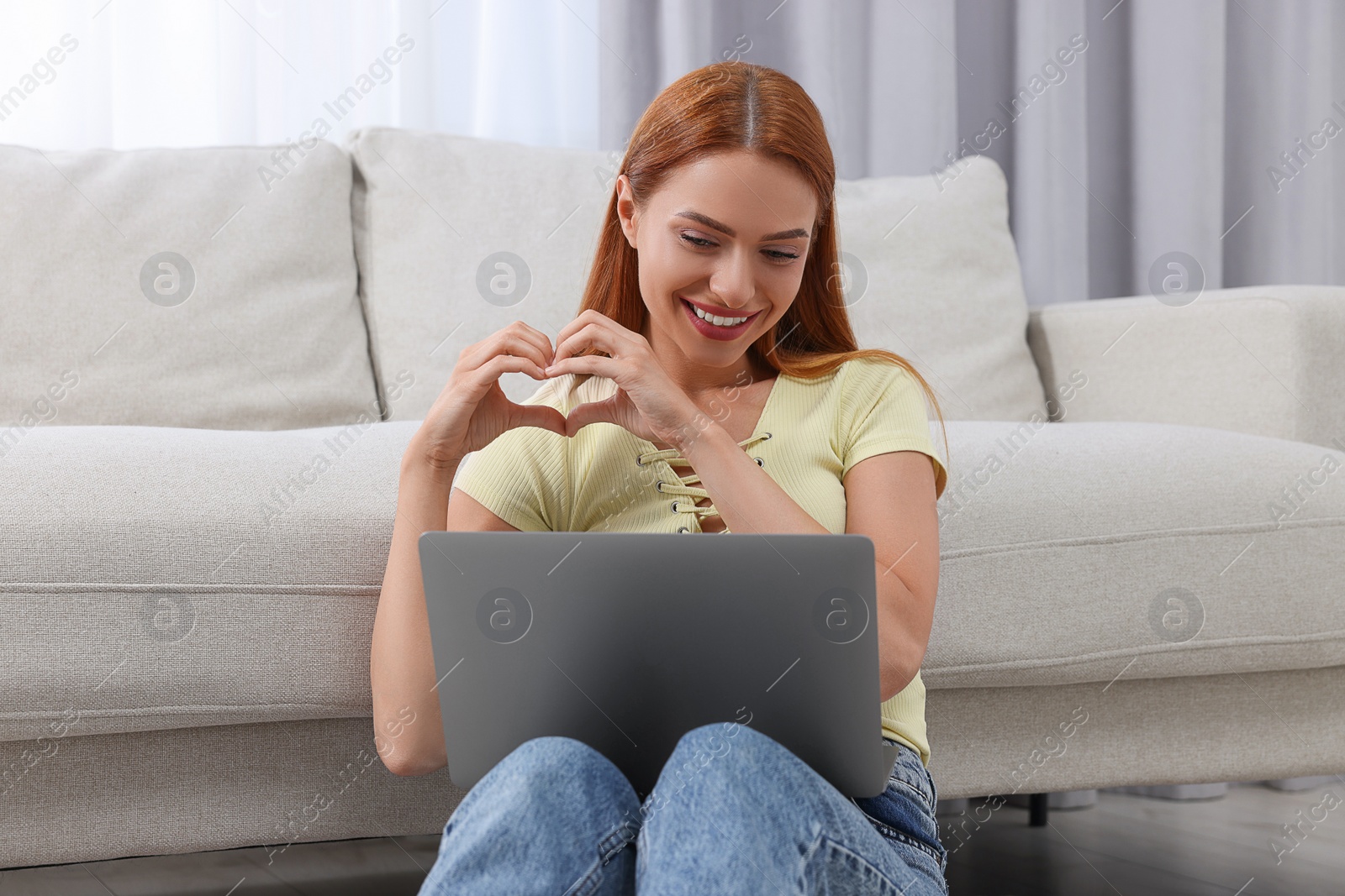 Photo of Woman making heart with hands during video chat via laptop at home. Long-distance relationship