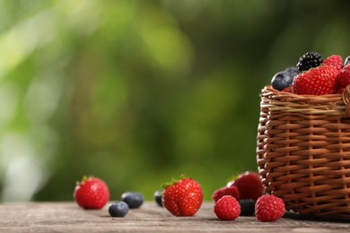 Wicker basket with different fresh ripe berries on wooden table outdoors, space for text