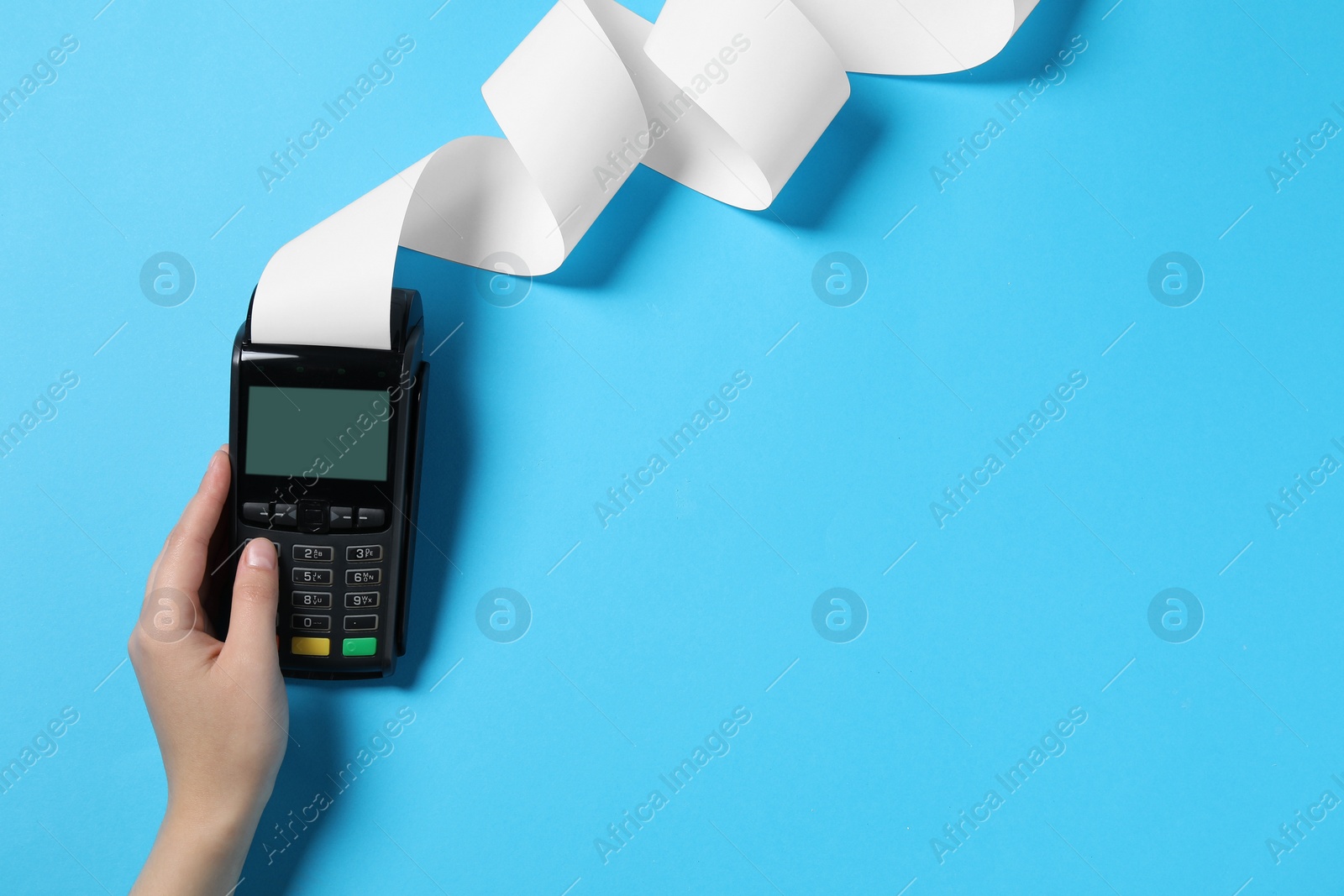 Photo of Woman using payment terminal with thermal paper for receipt on light blue background, top view. Space for text