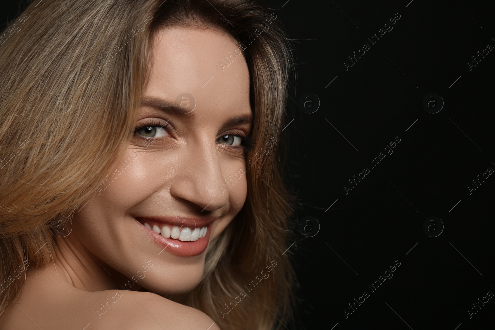 Photo of Portrait of happy young woman with beautiful blonde hair and charming smile on black background, closeup. Space for text