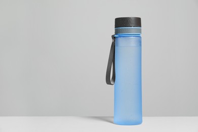 Photo of Stylish closed light blue bottle with water drops on white table, space for text