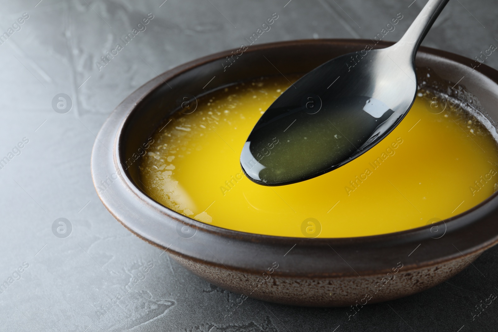 Photo of Spoon of clarified butter over bowl on black table, closeup