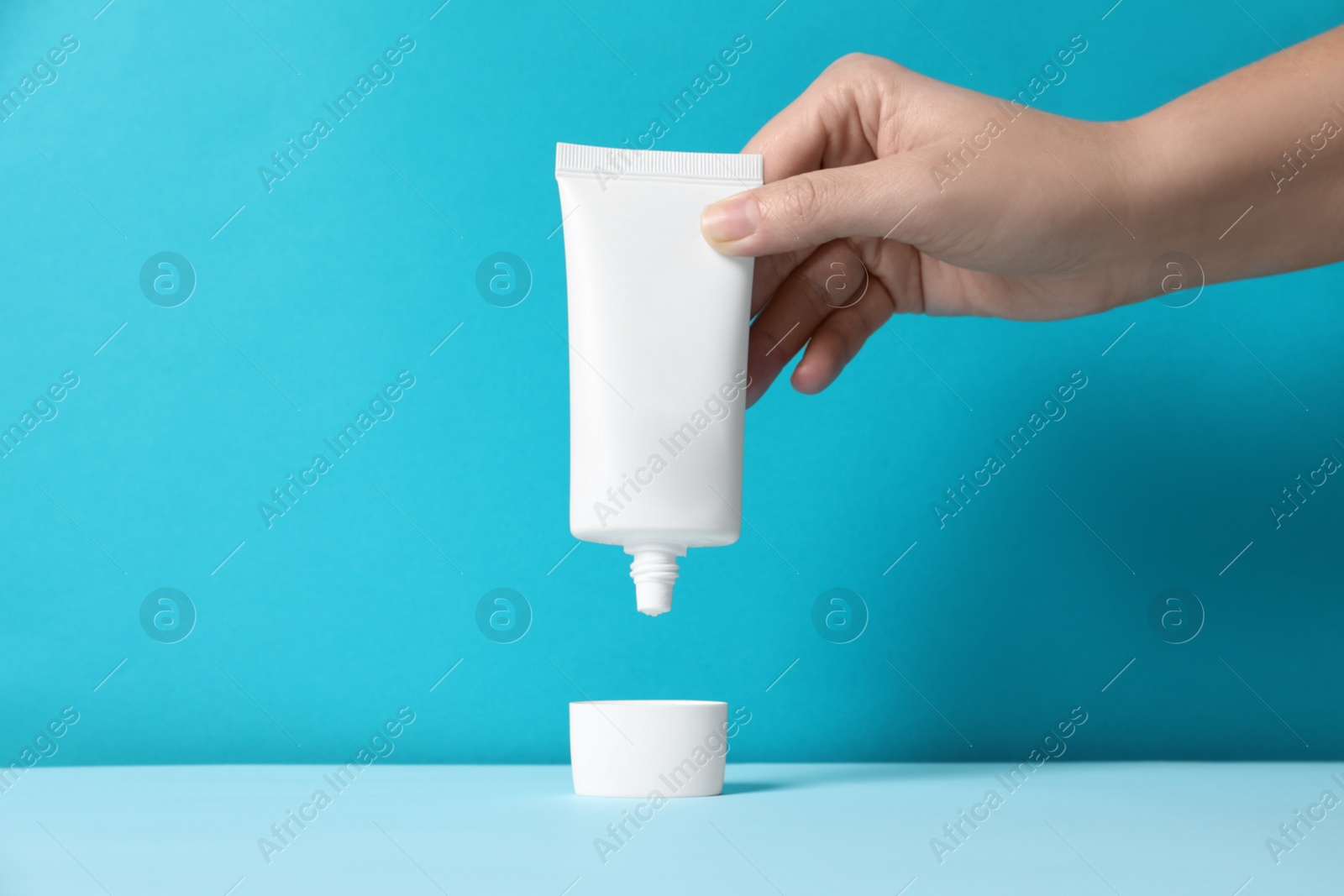 Photo of Woman with tube of hand cream at table against light blue background, closeup