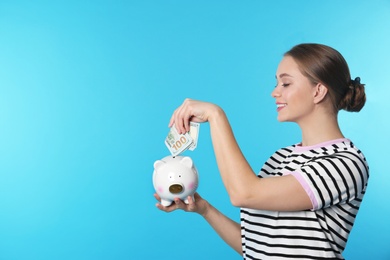 Photo of Happy young woman putting money into piggy bank on color background. Space for text