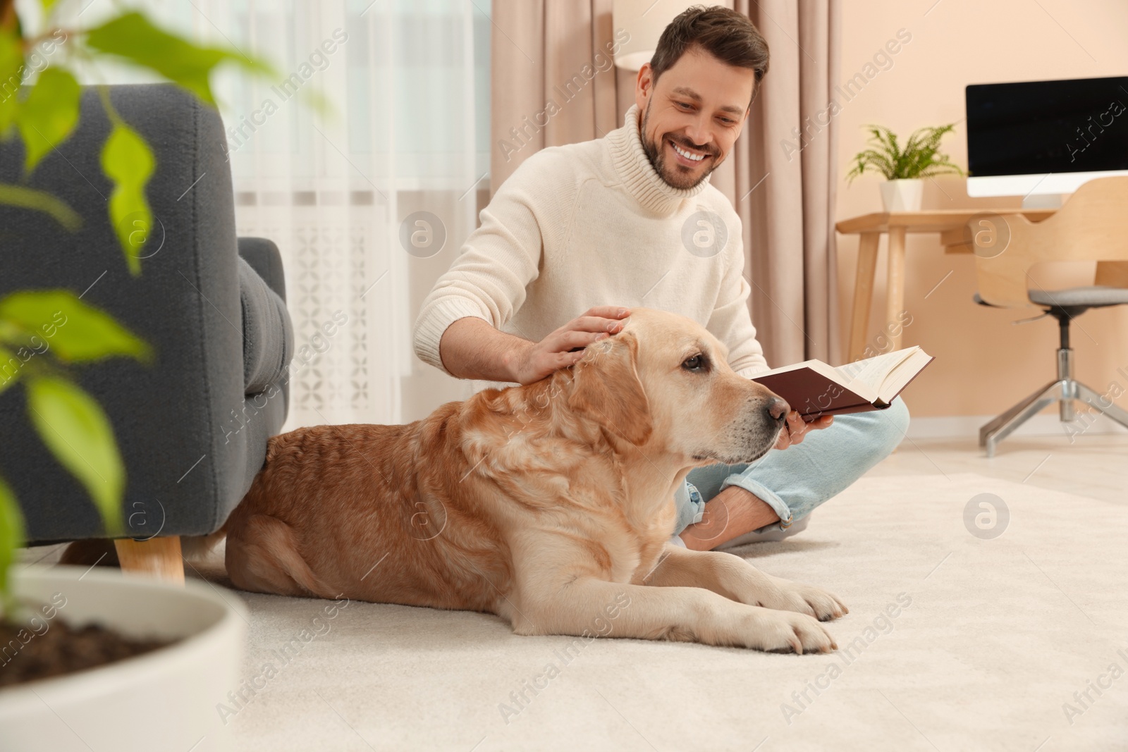 Photo of Man reading book on floor near his cute Labrador Retriever at home