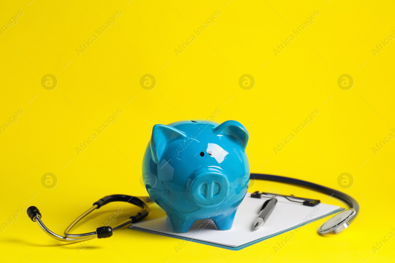 Photo of Piggy bank, stethoscope and clipboard on yellow background. Medical insurance