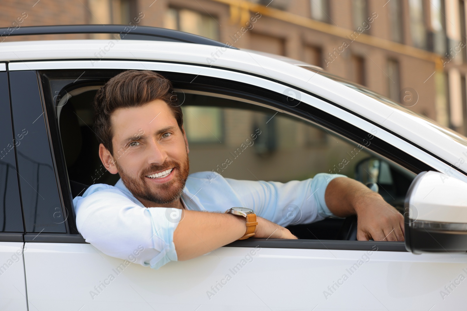 Photo of Happy bearded man looking out of car window on city street, view from outside. Enjoying trip