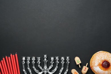 Hanukkah traditional menorah, candles, doughnut, dreidels with letters He, Pe, Nun, Gimel on black background, flat lay. Space for text