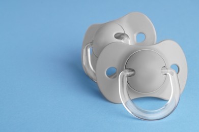 New baby pacifiers on light blue background, closeup. Space for text