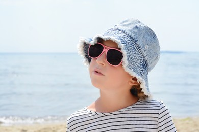 Photo of Little girl wearing sunglasses and hat at beach on sunny day. Space for text