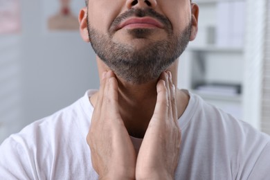 Endocrine system. Man doing thyroid self examination indoors, closeup