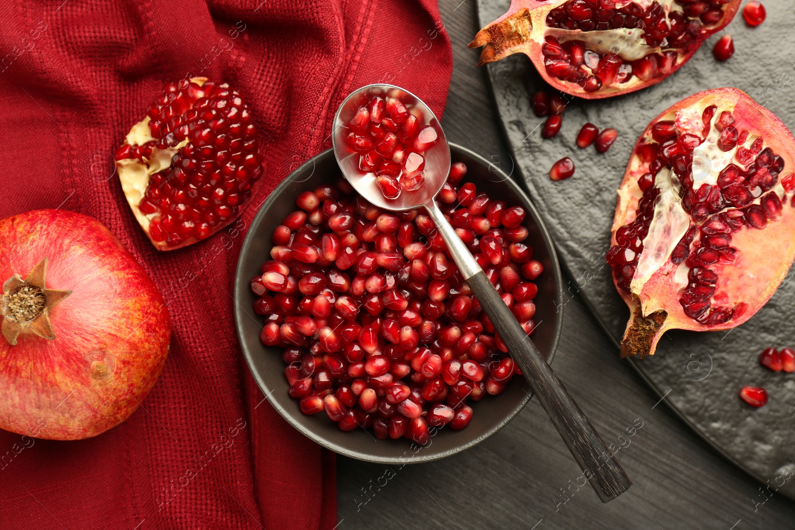 Photo of Tasty ripe pomegranates and grains on dark wooden table, flat lay