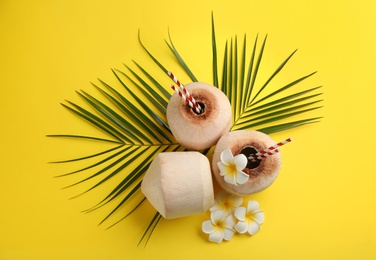Photo of Fresh coconuts with drinking straws and flowers on yellow background, flat lay