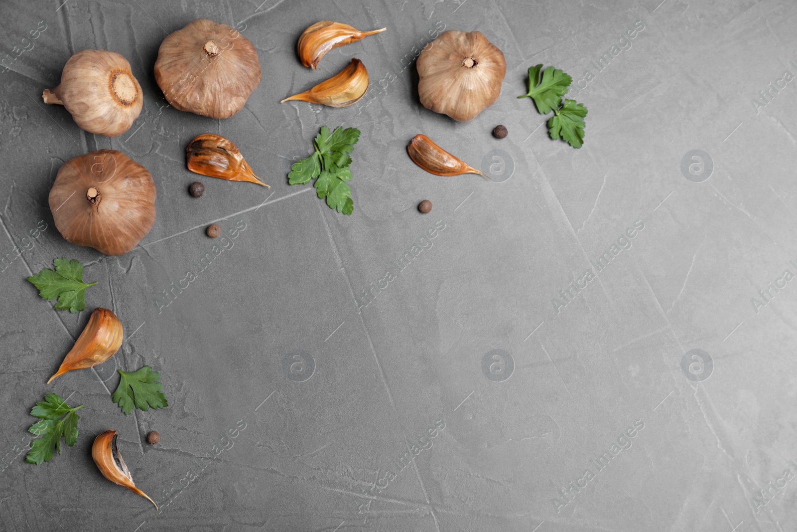 Photo of Flat lay composition with aged black garlic and parsley on gray background. Space for text