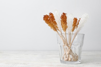 Photo of Sticks with sugar crystals in glass on white wooden table, space for text. Tasty rock candies