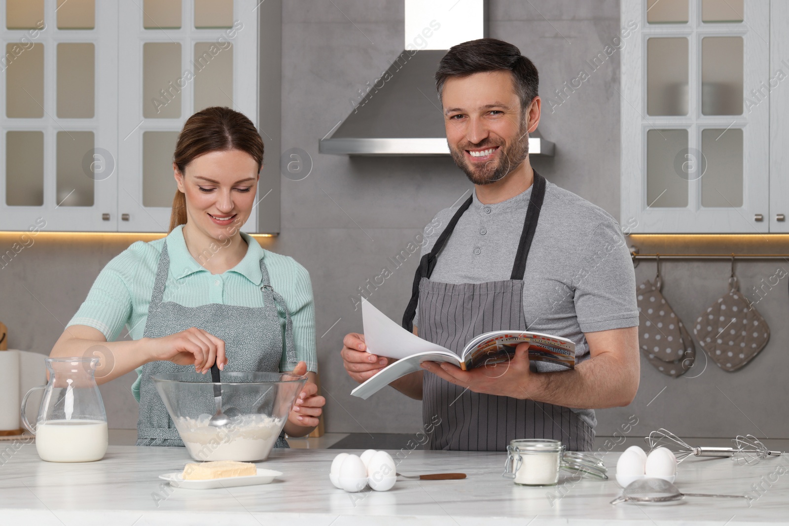 Photo of Happy couple reading recipe in culinary magazine while cooking at home