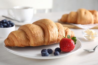 Plate with fresh crispy croissant and berries on white table