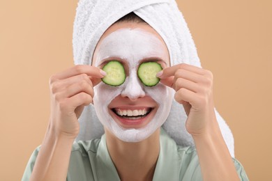 Photo of Woman with face mask and cucumber slices on beige background. Spa treatments