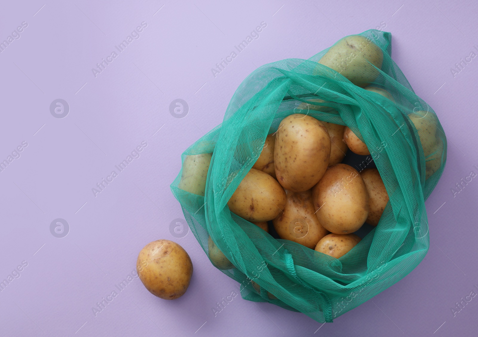 Photo of Net bag with potatoes on lilac background, top view