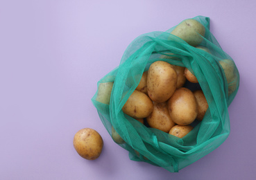 Photo of Net bag with potatoes on lilac background, top view