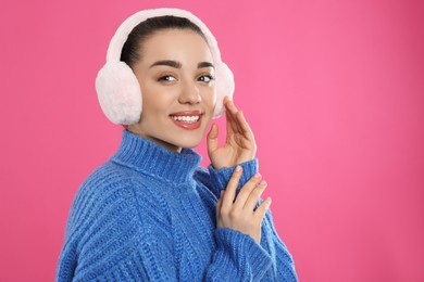 Photo of Beautiful young woman wearing earmuffs on pink background. Space for text