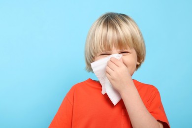 Photo of Boy blowing nose in tissue on light blue background, space for text. Cold symptoms