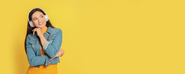 Image of Young woman listening to music with headphones on yellow background, space for text. Banner design