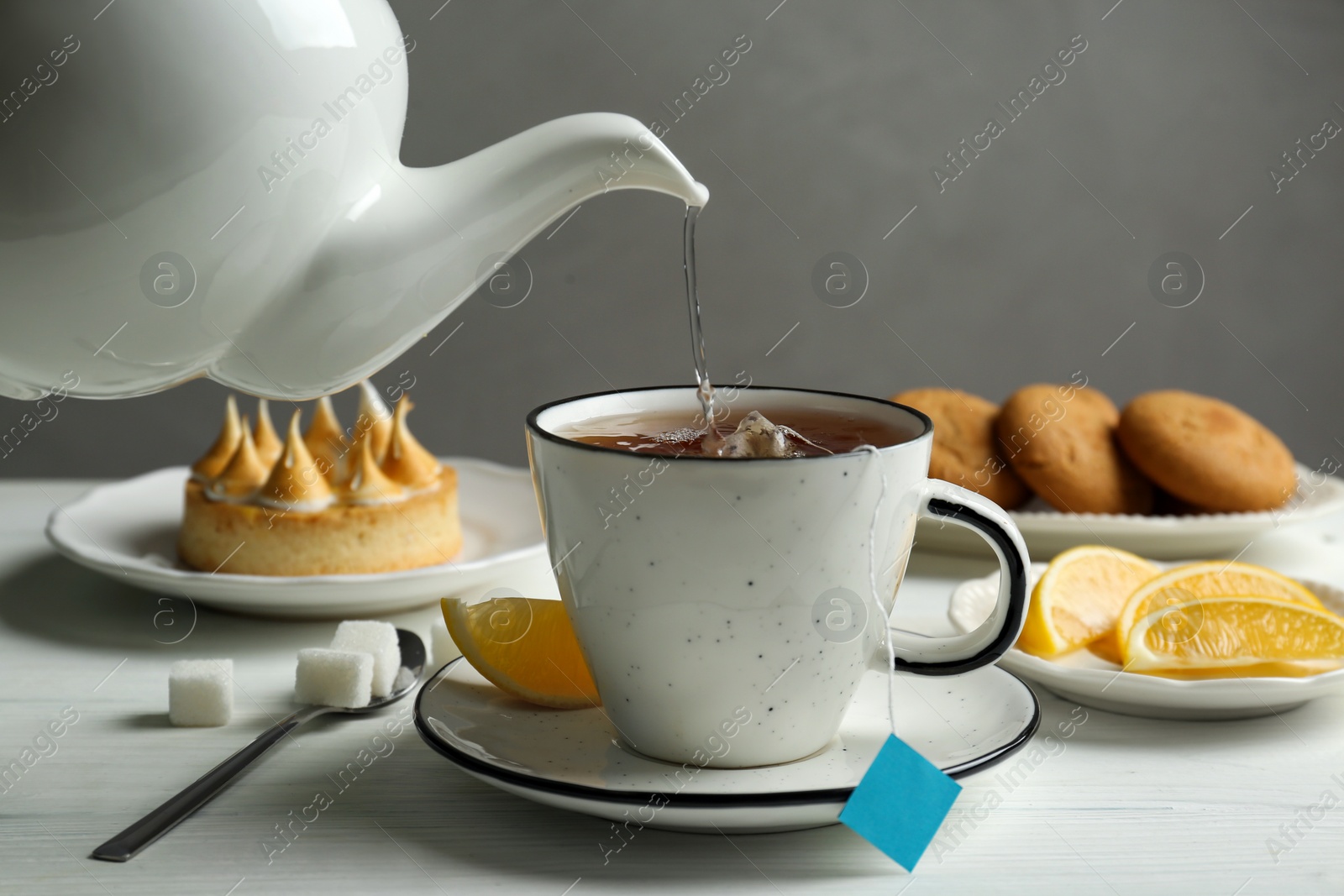 Photo of Pouring hot water into cup with tea bag at white wooden table