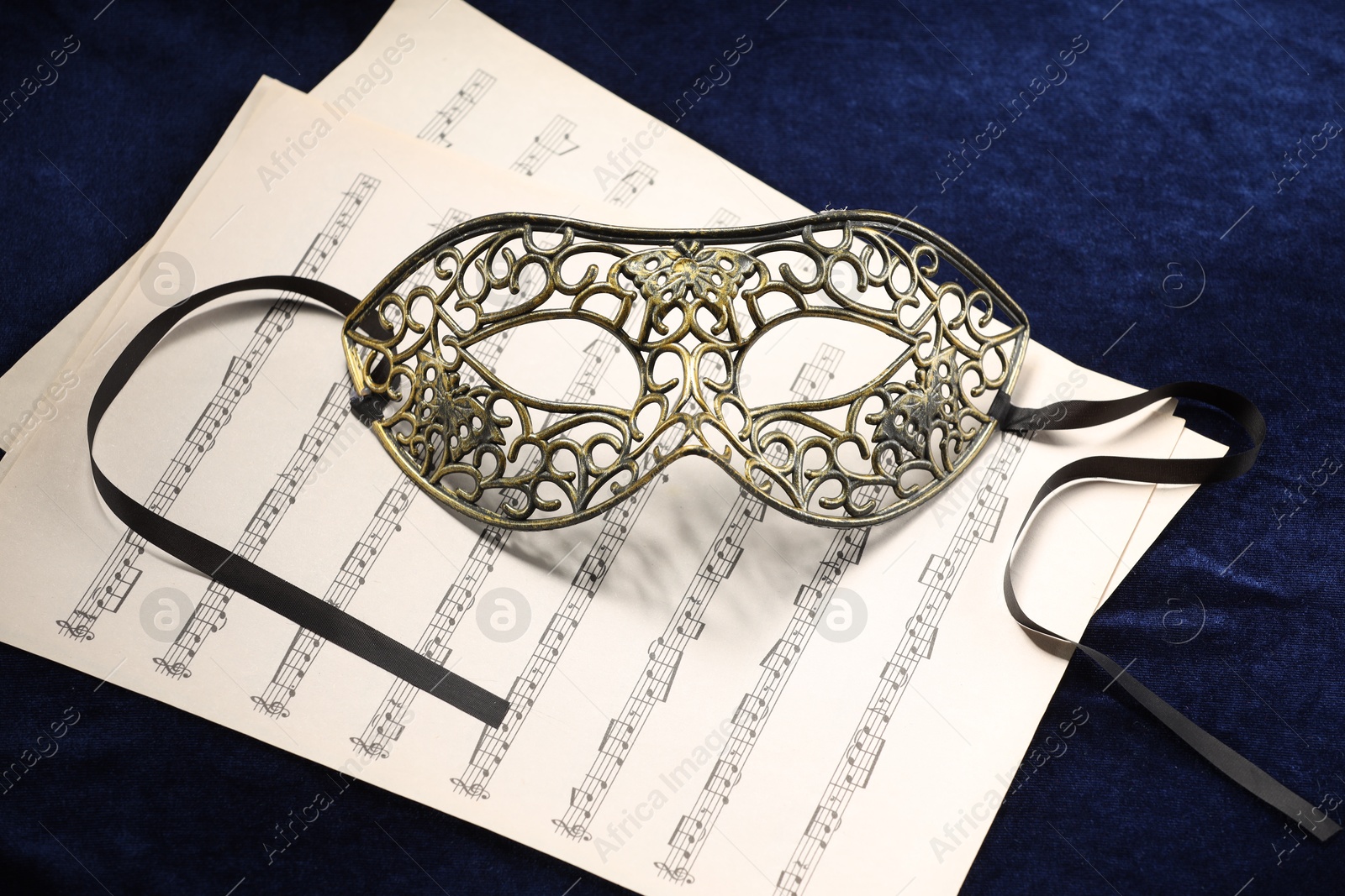 Photo of Elegant face mask and music sheets on blue fabric. Theatrical performance