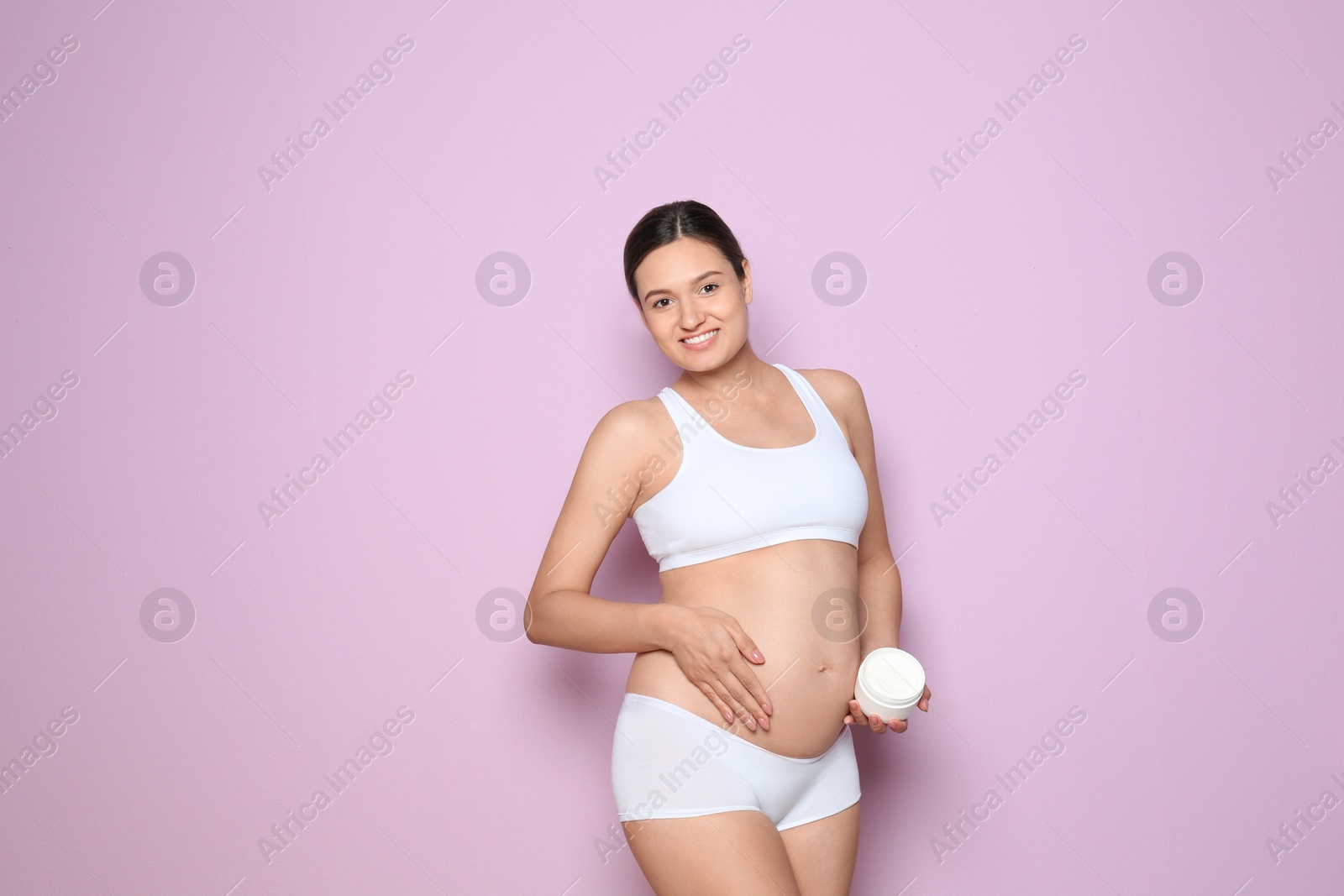 Photo of Pregnant woman holding body cream on color background