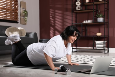 Overweight mature woman doing exercise while watching online class at home