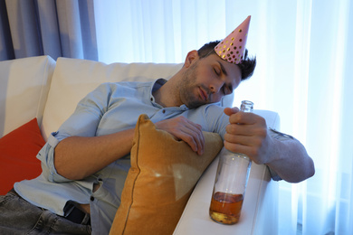 Photo of Young man with festive cap sleeping on sofa in room after party
