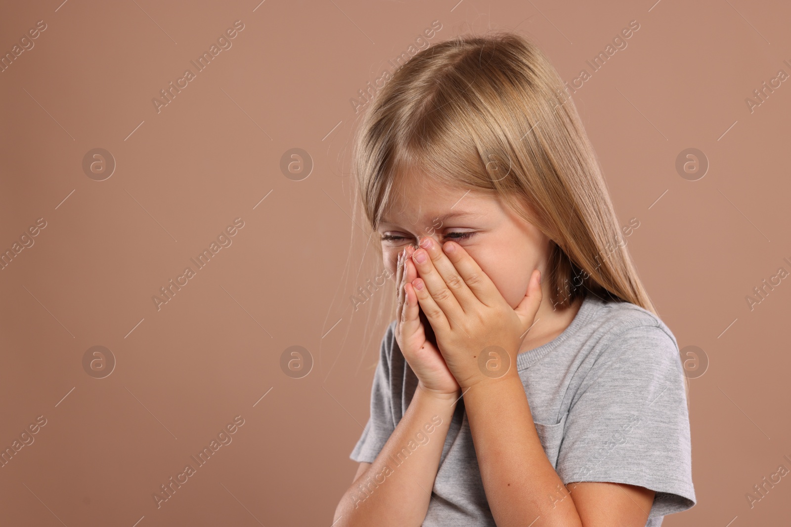 Photo of Suffering from allergy. Little girl sneezing on light brown background, space for text