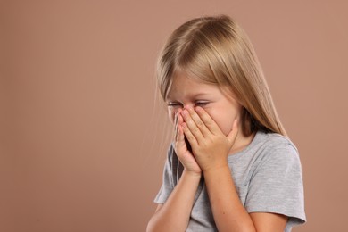 Suffering from allergy. Little girl sneezing on light brown background, space for text