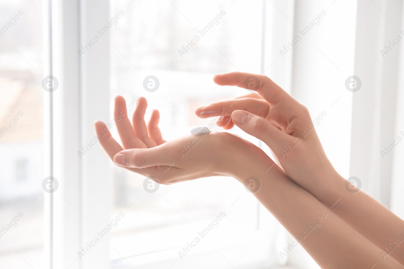 Photo of Young woman applying hand cream against window