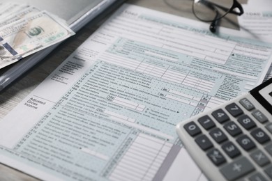Photo of Payroll. Tax return forms, dollar banknotes and calculator on table, selective focus