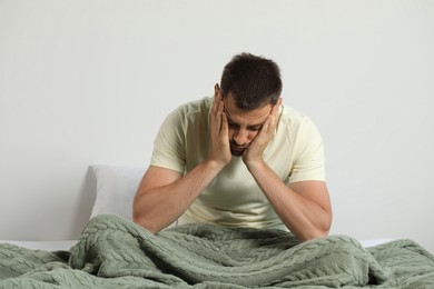 Photo of Sleep deprived man sitting on bed at home