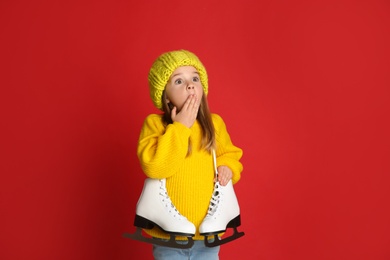 Photo of Surprised little girl in yellow knitted sweater with skates on red background