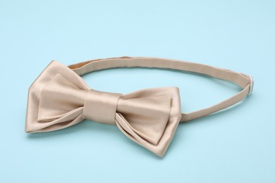 Stylish beige bow tie on light blue background, closeup
